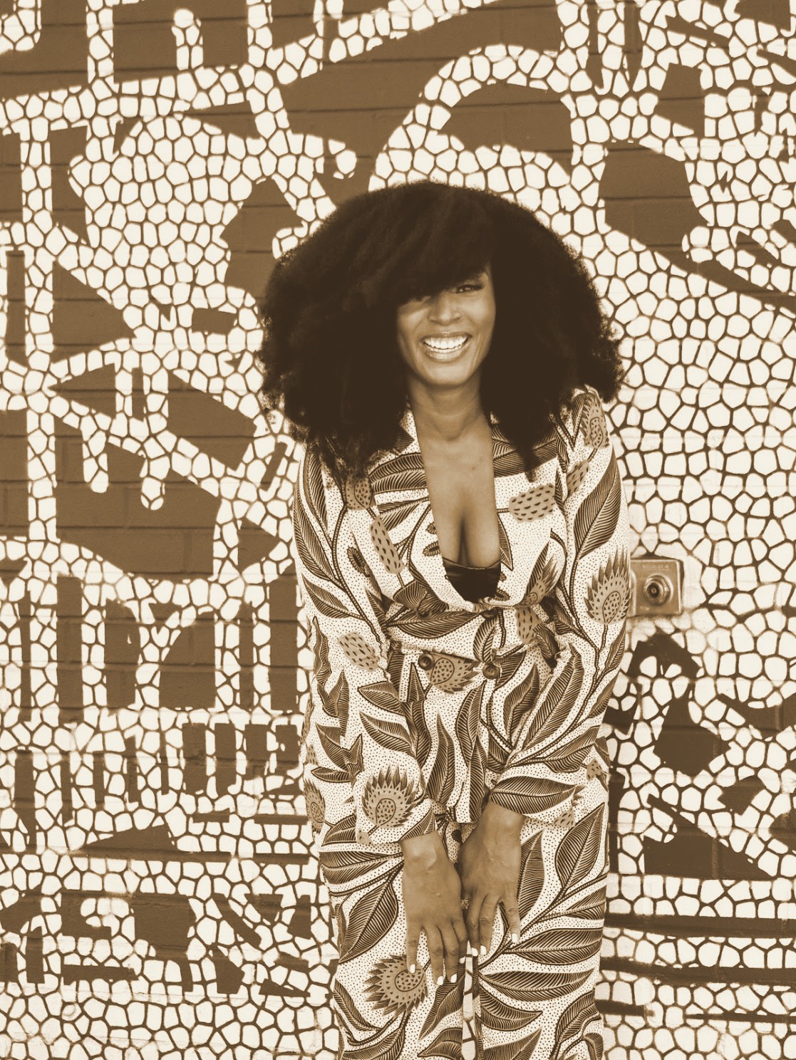 Dr. Kimberly Slaikeu, founder of BLVCK PAUSE, smiling in a patterned suit in front of a mural, in an espresso and bronze duotone